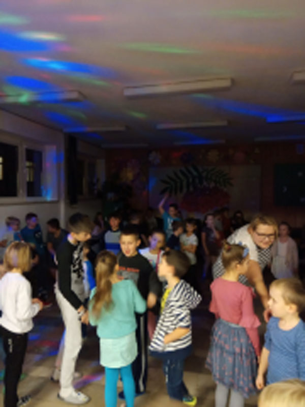 Uczniowie biorą udział w zabawach andrzejkowych, układają buty jeden za drugim, tańczą.