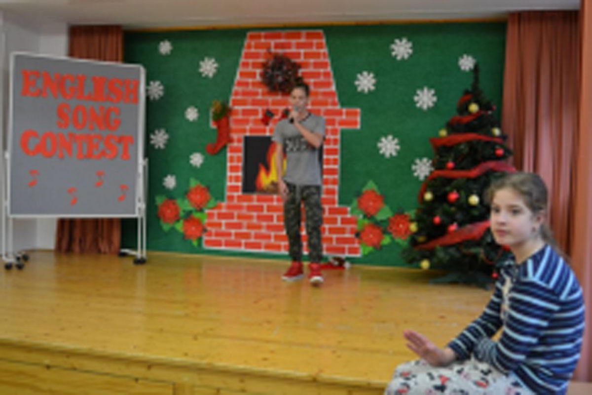 Uczniowie występują na scenie, trzymają mikrofony. Członkowie jury siedzą przy stoliku, wręczają dyplomy. Wspólne zdjęcie uczniów.