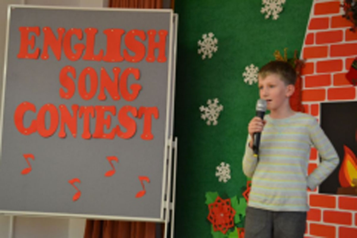 Uczniowie występują na scenie, trzymają mikrofony. Członkowie jury siedzą przy stoliku, wręczają dyplomy. Wspólne zdjęcie uczniów.