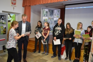 Zdjęcia przedstawiają salę, w której siedzą  uczniowie szkoły i oglądają prezentację.  Z frontu wystawione są stelaże, na których przypięte są zdjęcia przedstawiające Żołnierzy Wyklętych. Na jednym ze zdjęć przedstawiony jest dyrektor szkoły i nauczycielk