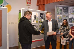 Zdjęcia przedstawiają salę, w której siedzą  uczniowie szkoły i oglądają prezentację.  Z frontu wystawione są stelaże, na których przypięte są zdjęcia przedstawiające Żołnierzy Wyklętych. Na jednym ze zdjęć przedstawiony jest dyrektor szkoły i nauczycielk