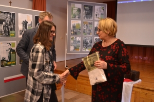 Zdjęcia przedstawiają salę, w której siedzą  uczniowie szkoły i oglądają prezentację.  Z frontu wystawione są stelaże, na których przypięte są zdjęcia przedstawiające Żołnierzy Wyklętych. Na jednym ze zdjęć przedstawiony jest dyrektor szkoły i nauczycielk