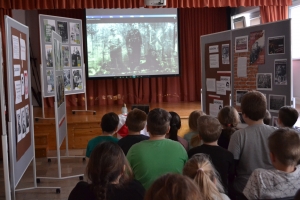 Zdjęcia przedstawiają salę, w której siedzą  uczniowie szkoły i oglądają prezentację.  Z frontu wystawione są stelaże, na których przypięte są zdjęcia przedstawiające Żołnierzy Wyklętych. Na jednym ze zdjęć przedstawiony jest dyrektor szkoły i nauczycielk
