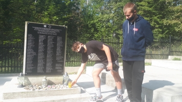 Uczniowie przy nagrobkach zapalają znicze.