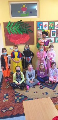 Grupa dzieci, przebranych w stroje bajkowych postaci  siedzą na dywanie i słuchają czytanej im bajki.