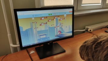 Uczniowie przy komputerach i stolikach. Układają wierze z plastikowych kubków, losują łyżeczki z zadaniami, grają w gry planszowe, rozwiązują zadania w programie komputerowym.