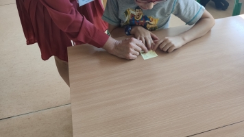 Uczniowie przy komputerach i stolikach. Układają wierze z plastikowych kubków, losują łyżeczki z zadaniami, grają w gry planszowe, rozwiązują zadania w programie komputerowym.