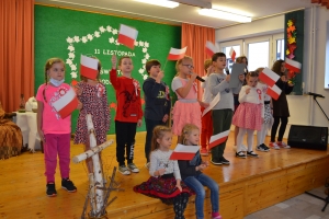 Uczniowie na scenie śpiewają pieśni. Koło sceny poczet sztandarowy, na scenie uczniowie przebrani w czarne stroje zaborców i  na biało za orła. Uczniowie składają znicze pod krzyżem.