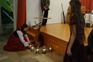 Uczniowie na scenie śpiewają pieśni. Koło sceny poczet sztandarowy, na scenie uczniowie przebrani w czarne stroje zaborców i  na biało za orła. Uczniowie składają znicze pod krzyżem.