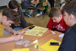 Uczniowie przy stolikach, rozwiązują krzyżówki, wykreślanki, rebusy.