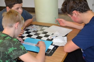 Uczniowie przy stolikach, rozwiązują krzyżówki, wykreślanki, rebusy.