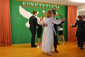 Uczniowie na scenie. Przebrani w stroje biało czarne i ułańskie z epoki. Tańczą, markują ruchy kopania, ogrzewania przy ognisku.