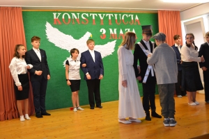 Uczniowie na scenie. Przebrani w stroje biało czarne i ułańskie z epoki. Tańczą, markują ruchy kopania, ogrzewania przy ognisku.