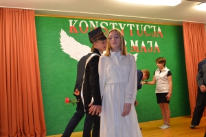 Uczniowie na scenie. Przebrani w stroje biało czarne i ułańskie z epoki. Tańczą, markują ruchy kopania, ogrzewania przy ognisku.