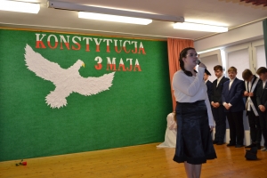 Uczniowie na scenie. Przebrani w stroje biało czarne i ułańskie z epoki. Tańczą, markują ruchy kopania, ogrzewania przy ognisku.