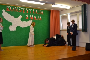 Uczniowie na scenie. Przebrani w stroje biało czarne i ułańskie z epoki. Tańczą, markują ruchy kopania, ogrzewania przy ognisku.