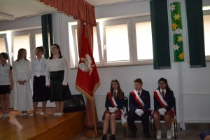 Uczniowie na scenie. Przebrani w stroje biało czarne i ułańskie z epoki. Tańczą, markują ruchy kopania, ogrzewania przy ognisku.