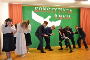 Uczniowie na scenie. Przebrani w stroje biało czarne i ułańskie z epoki. Tańczą, markują ruchy kopania, ogrzewania przy ognisku.