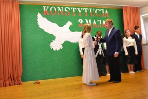 Uczniowie na scenie. Przebrani w stroje biało czarne i ułańskie z epoki. Tańczą, markują ruchy kopania, ogrzewania przy ognisku.