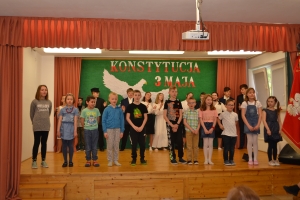 Uczniowie na scenie. Przebrani w stroje biało czarne i ułańskie z epoki. Tańczą, markują ruchy kopania, ogrzewania przy ognisku.