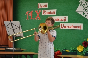 Uczniowie występują na scenie w galowych strojach, dyrektor pasuje uczniów długim ołówkiem