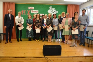 Uczniowie występują na scenie w galowych strojach, dyrektor pasuje uczniów długim ołówkiem