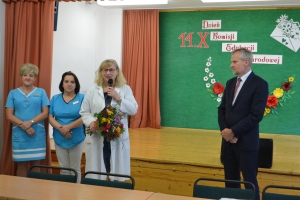 Uczniowie występują na scenie w galowych strojach, dyrektor pasuje uczniów długim ołówkiem