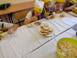 dzieci ubrane w fartuszki i czapki kucharskie, kroją warzywa