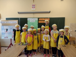 dzieci ubrane w fartuszki i czapki kucharskie, kroją warzywa