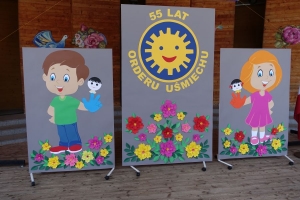 Występujący na scenie tańczą z pomponami, ze wstęgami. Na scenie dekoracja, pacynki Jacek i Agatka. Order Uśmiechu wręcza sekretarz Kapituły Orderu Uśmiechu i państwo Burcanowie.