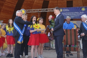 Występujący na scenie tańczą z pomponami, ze wstęgami. Na scenie dekoracja, pacynki Jacek i Agatka. Order Uśmiechu wręcza sekretarz Kapituły Orderu Uśmiechu i państwo Burcanowie.